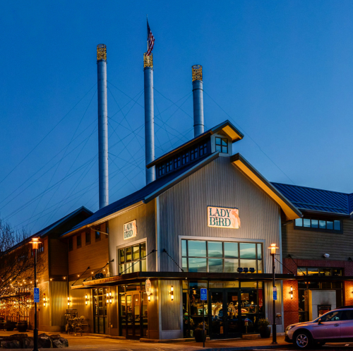 Exterior of Lady Bird restaurant at dusk, featuring three tall smokestacks and warm lighting.